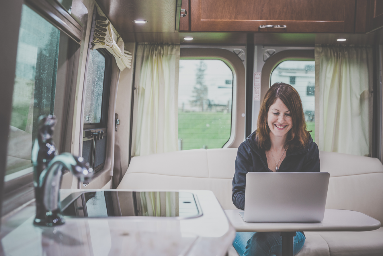 Young Woman Using a Laptop Inside a luxury Motorhome on a campground on a rainy day. 
