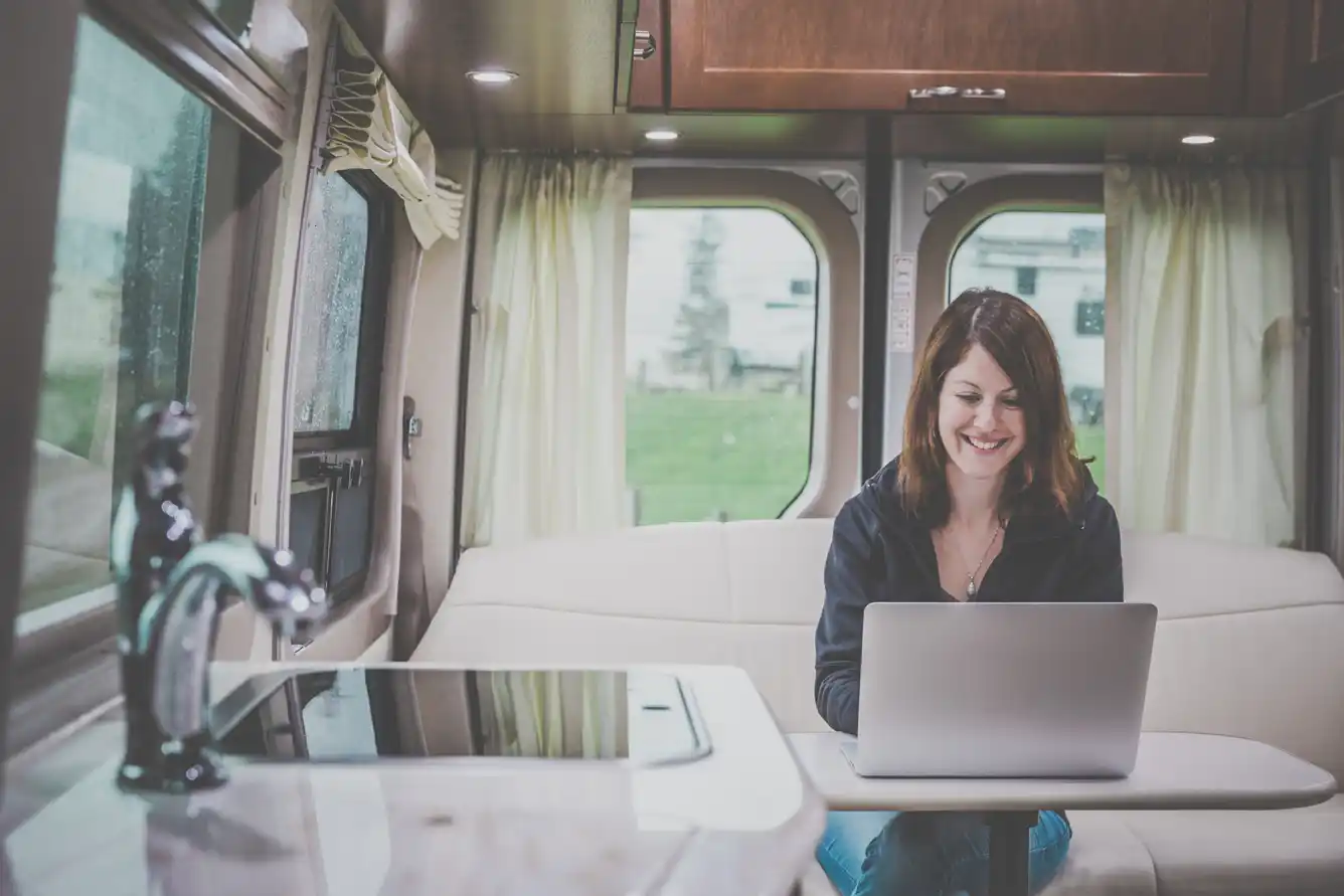 Young woman using a laptop inside a luxury motorhome on a campground on a rainy day.