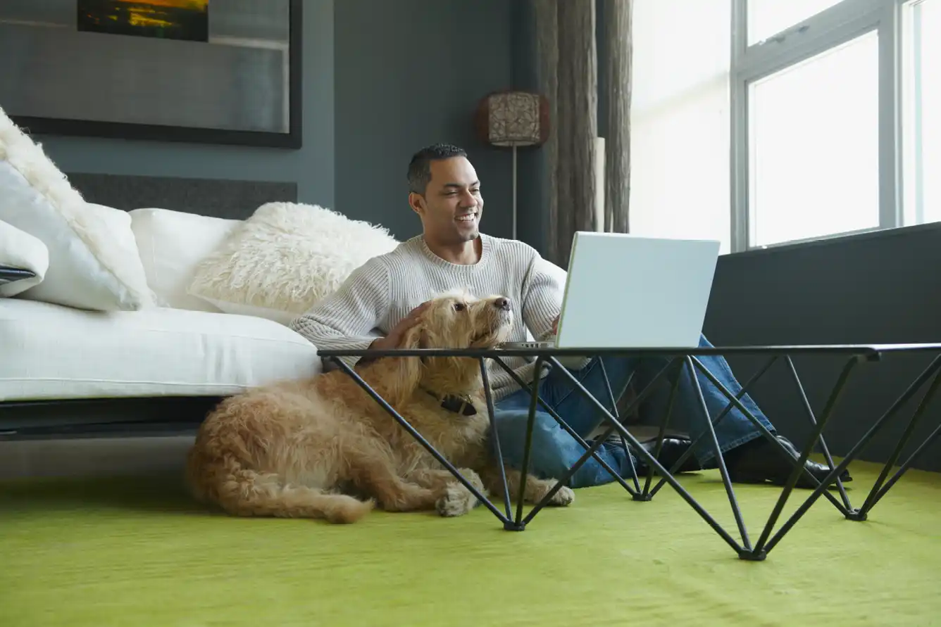 Man using laptop as dog sits nearby in an apartment.