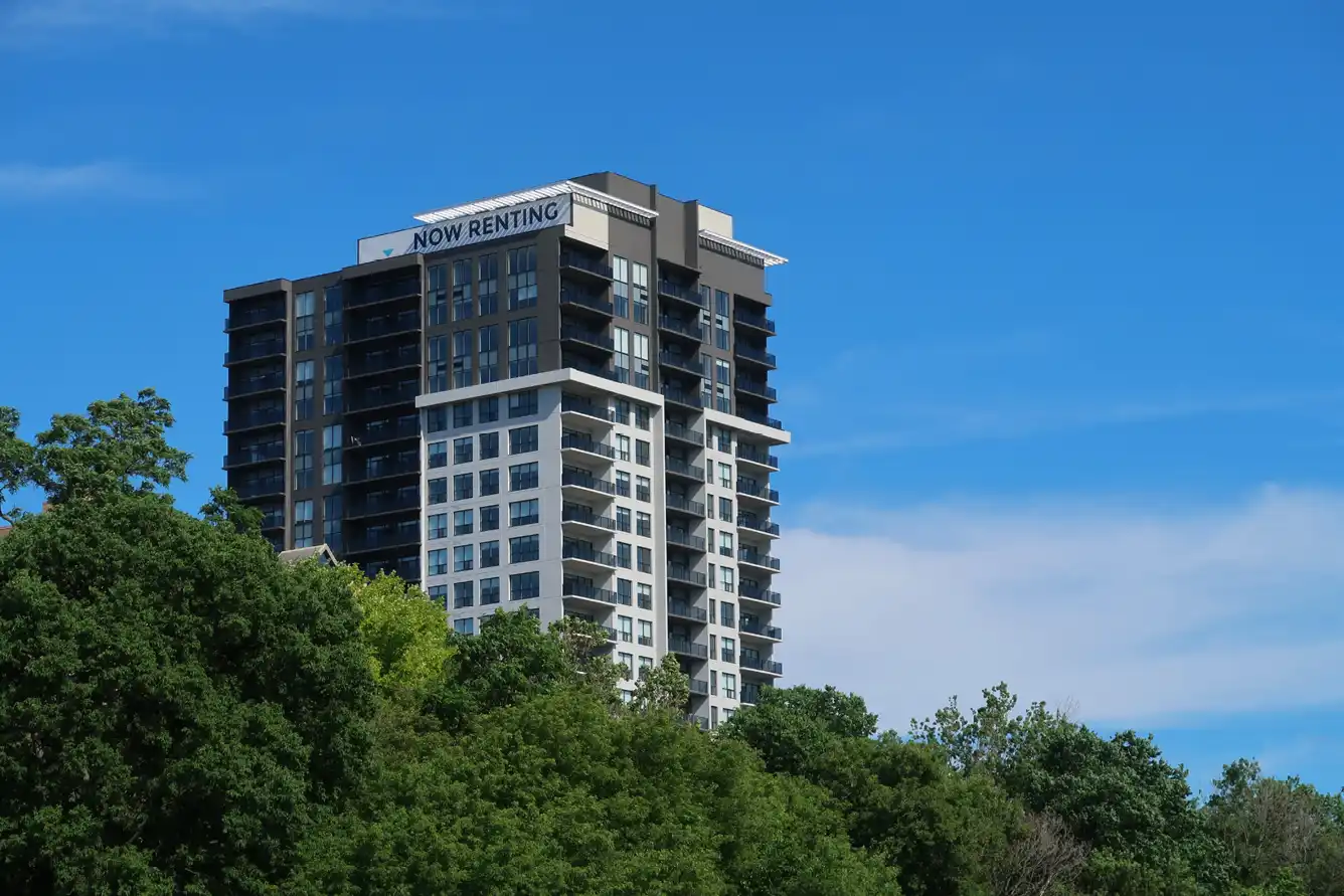 A tall residential tower with banner stating 'now renting', against blue sky.