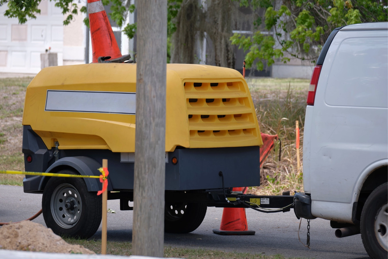 Utility van with yellow compressor trailer with a jackhammer machine.