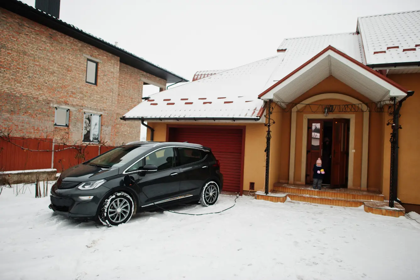 Electric vehicle charging outside a snow-covered house - winter-proofing your home and auto