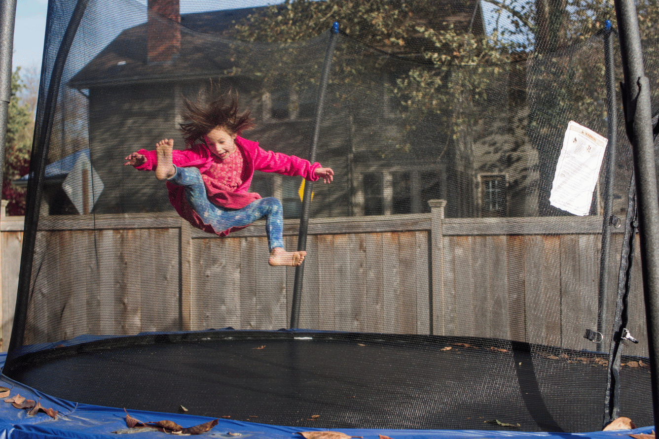 A child joyfully jumping on a trampoline, with hair flying due to the movement, surrounded by a safety net.