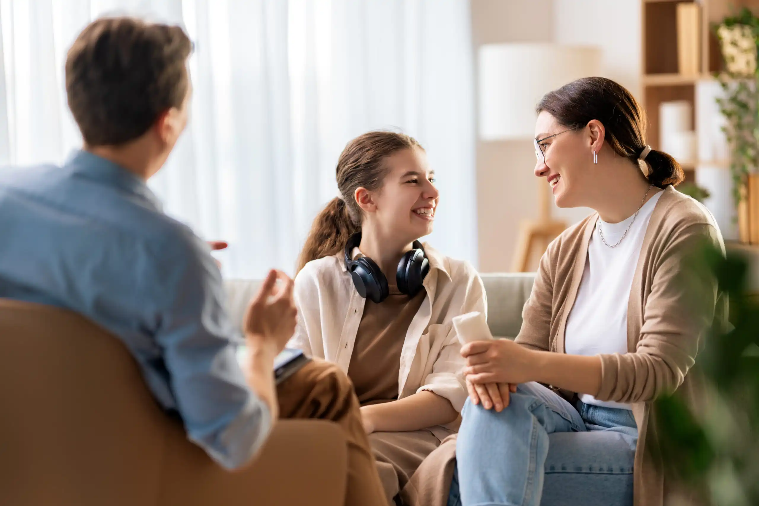 A family sitting together at home, warmly engaging in conversation with their teenage daughter—representing trust, communication, and supportive parenting.