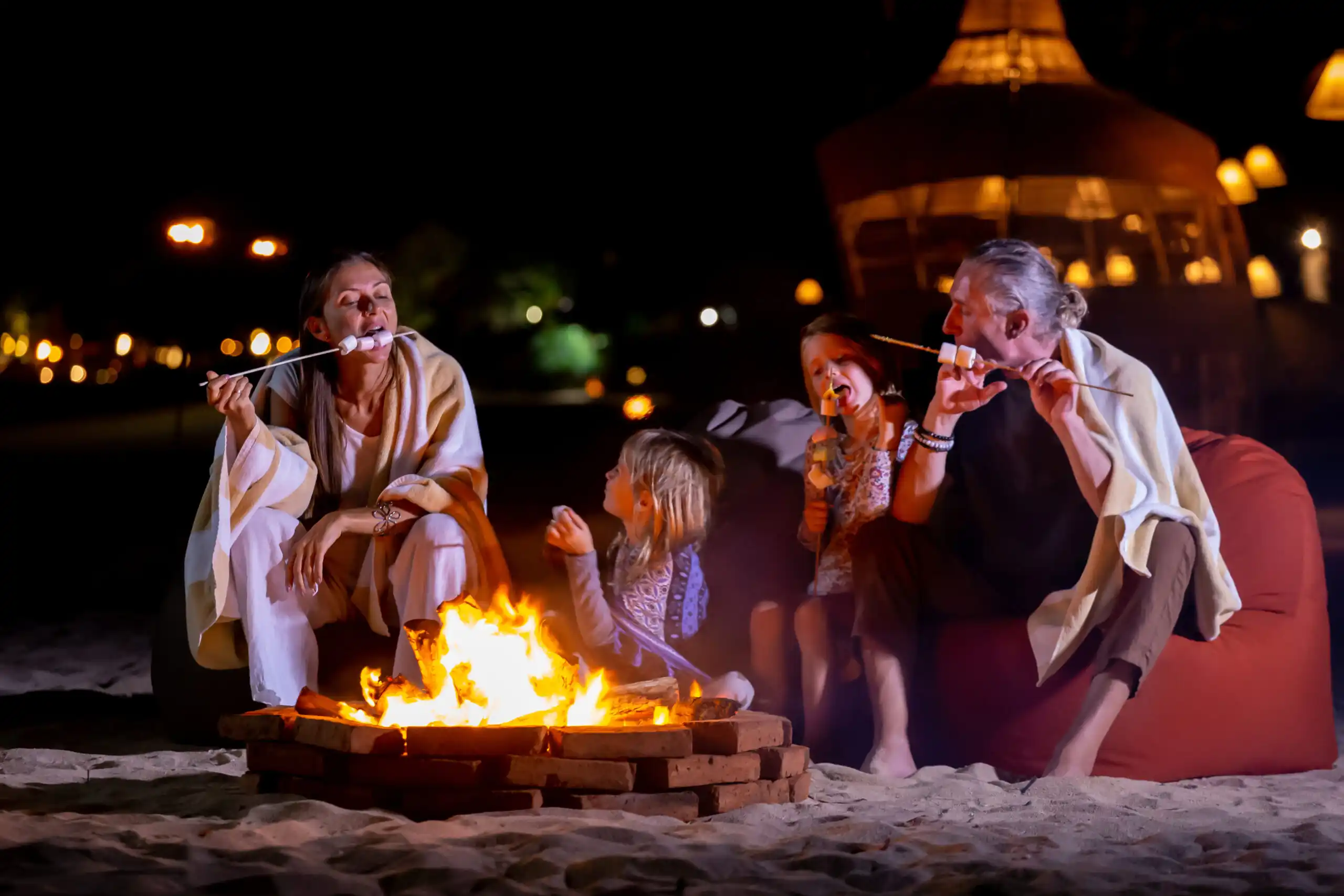 Happy family gathered around a glowing bonfire, toasting marshmallows under the stars near their cozy cottage—capturing the warmth and memories that cottage insurance helps protect.