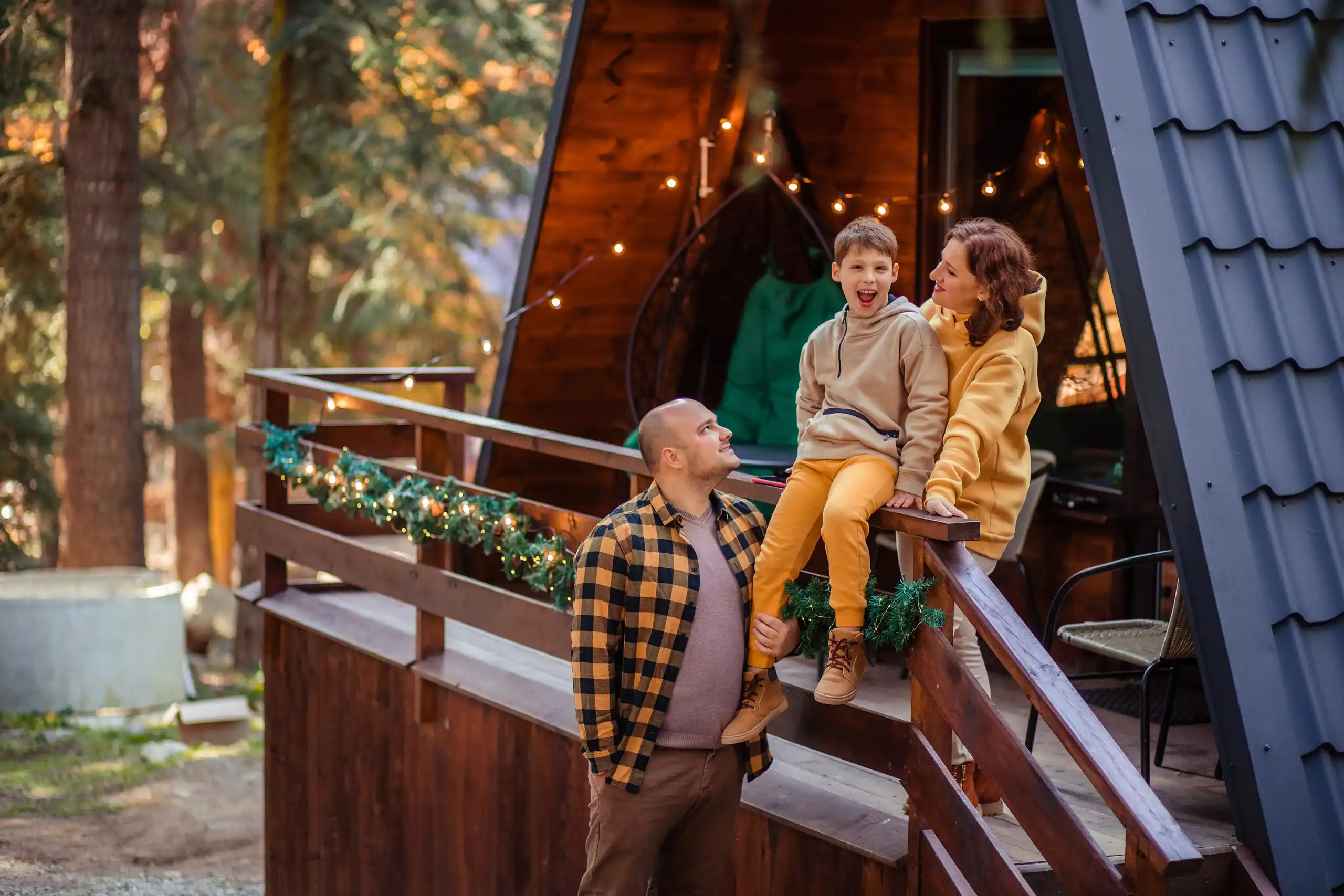 Smiling family enjoying time together in a forested mountain setting near a well-maintained wooden cottage, highlighting the importance of protecting cherished vacation homes with reliable cottage insurance.