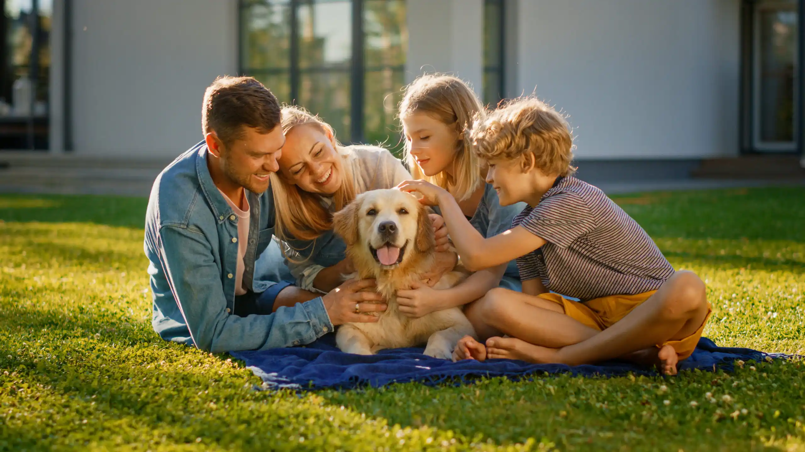 Smiling portrait of a joyful family of four enjoying a sunny picnic on a lush green lawn, lovingly posing with their happy pet dog — a scene that reflects the peace of mind and ease that comes with having pet insurance.