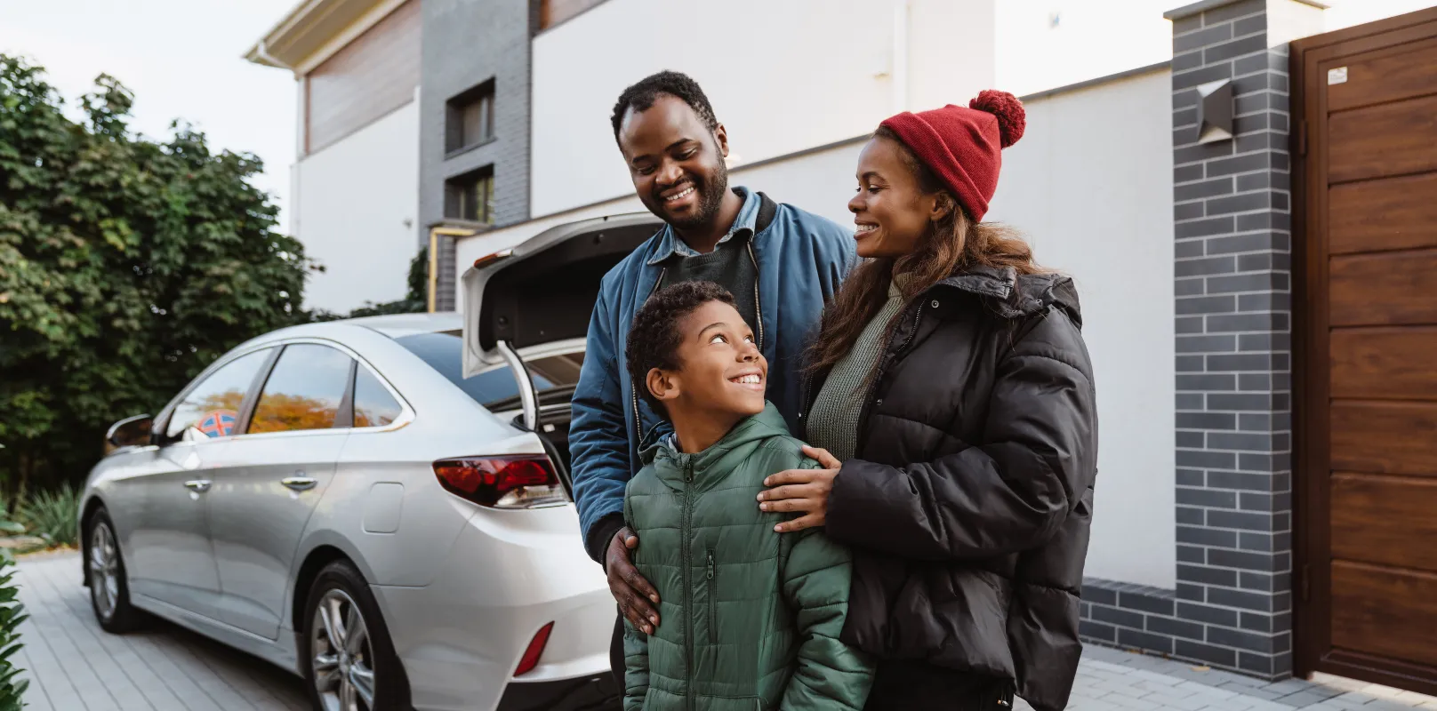 Family standing in front of a car, smiling and chatting together.