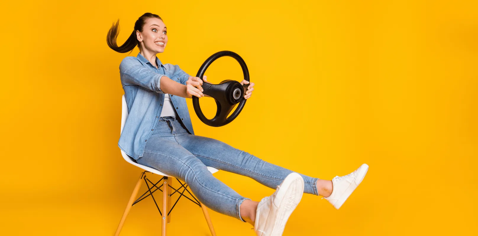 Person seated on a chair holding a steering wheel, symbolizing learning, practicing, or preparing to drive.