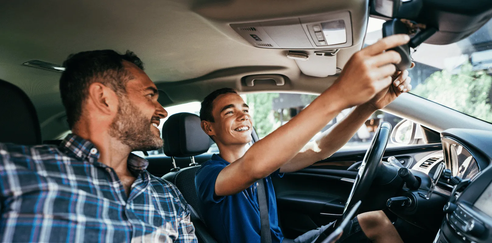 Young driver seated in the driver’s seat adjusting the rearview mirror while another person sits in the front passenger seat.