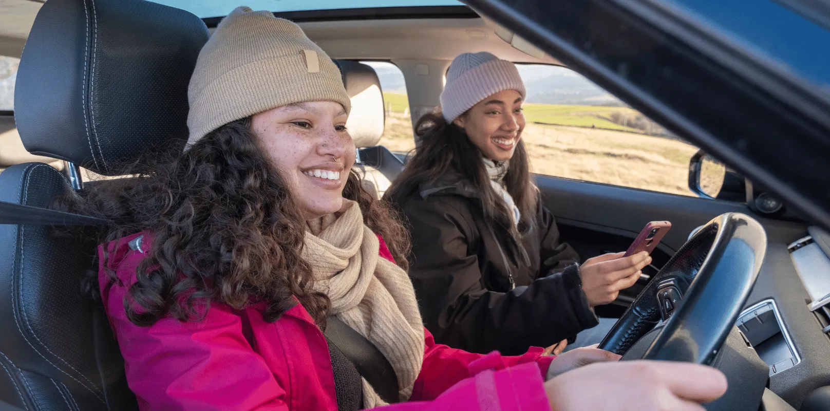 Driver seated behind the wheel of a vehicle with a passenger in the front seat during a daytime drive.