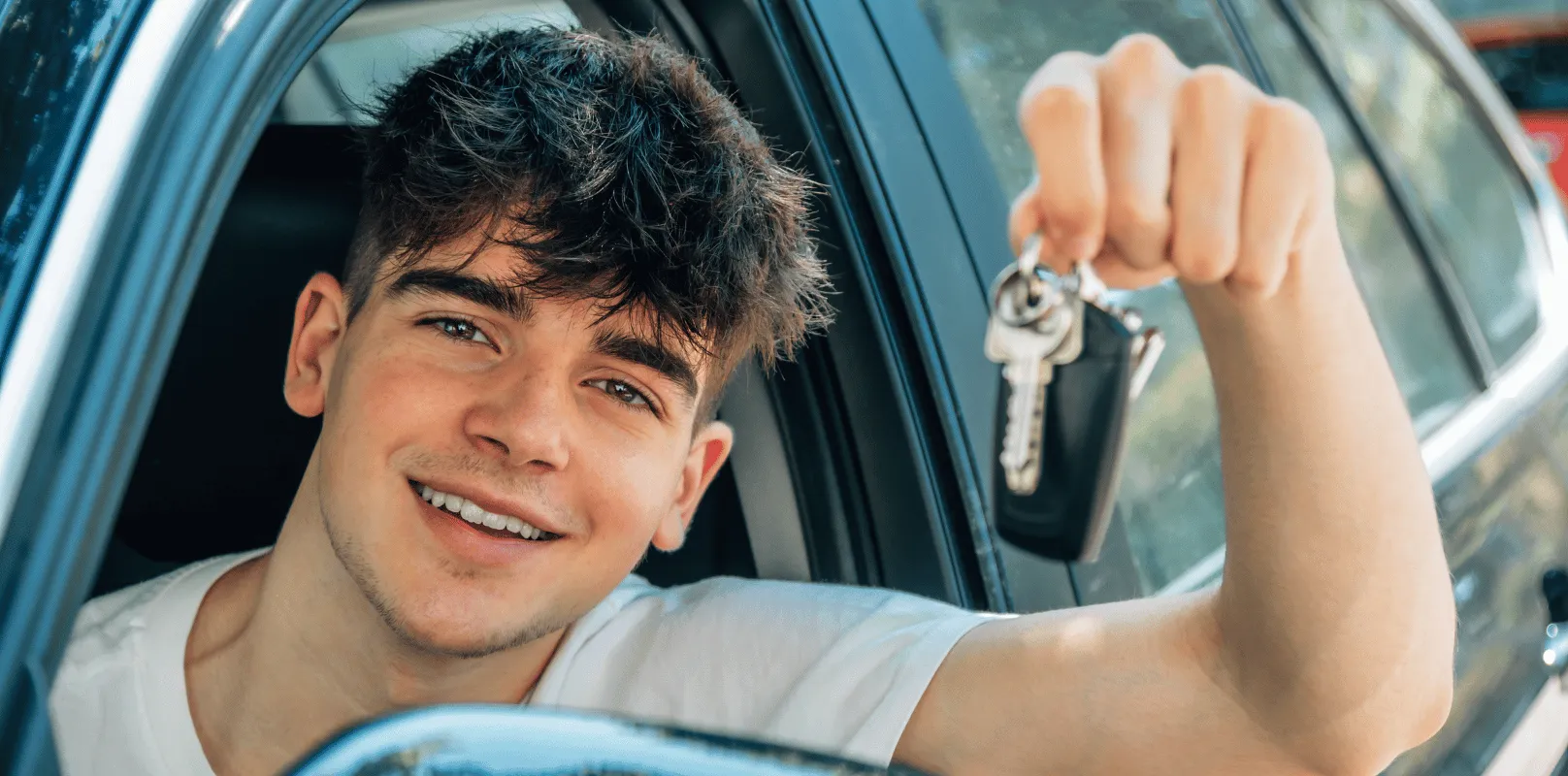 Driver leaning out of a vehicle window holding a set of car keys inside a parked car.