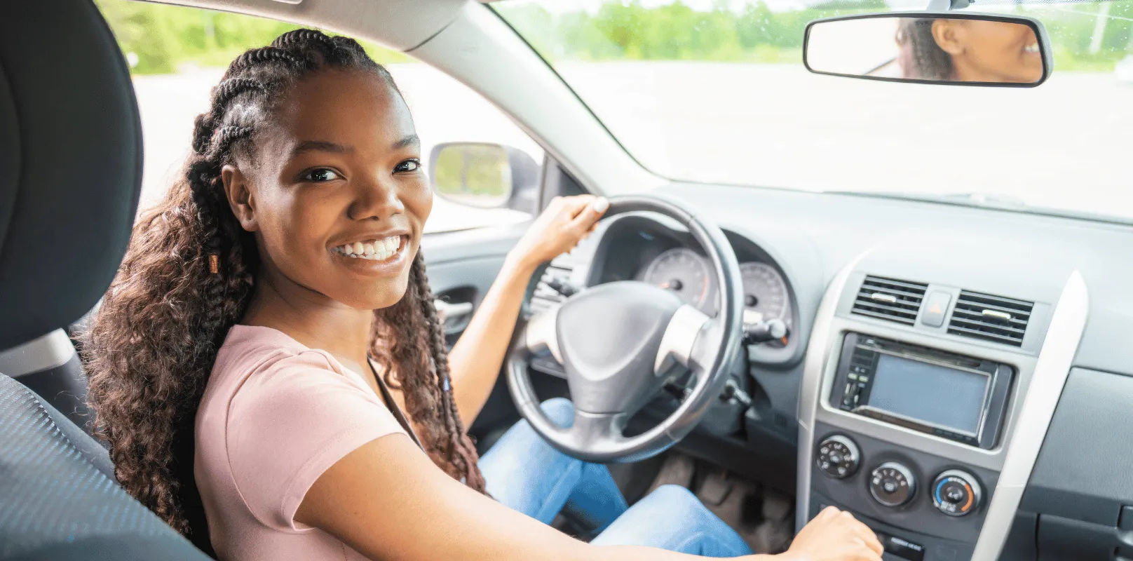 Driver seated behind the steering wheel inside a vehicle, preparing to operate the car. <br />